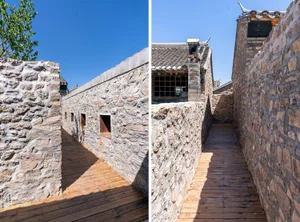 A wooden path between tall stone walls under a clear blue sky.