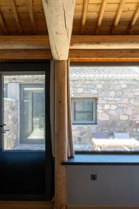 A rustic kitchen with stone walls, wooden beams, and glass windows.