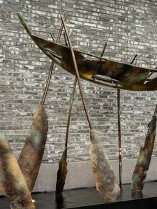 A bronze abstract sculpture with crossed metal rods and water elements in front of a brick wall.