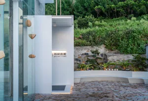 A minimalist entranceway with concrete walls and a stone pathway leading to a green landscape.