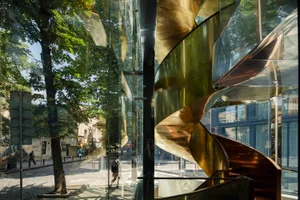 A modern building with spiral glass staircase in a sunny urban setting.