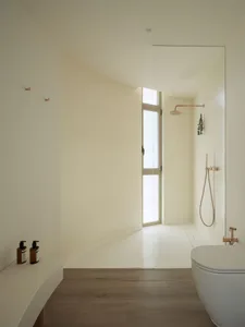 A modern bathroom featuring white marble walls and floor, with a white bathtub and wooden flooring.