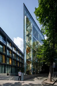 A modern office building with a glass and concrete exterior, featuring a spiral staircase and a nearby tree.