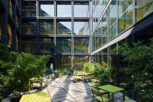 An indoor green space with modern furniture, glass walls, and potted plants.