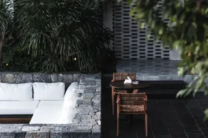 A modern interior space featuring a white sectional sofa, a wooden table with a book and small plant, and a wall made of natu
