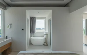 Modern minimalist bedroom featuring a white wall and a white bathtub with a window overlooking the beach.