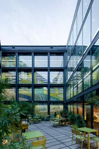 Outdoor patio area inside an office building with glass walls, featuring tables, chairs, and greenery.