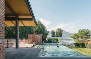 People enjoying a modern residential swimming pool in an outdoor space surrounded by greenery and mountains.