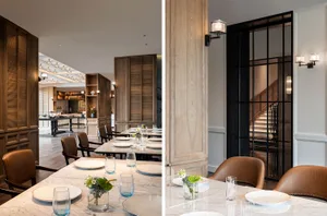 Modern restaurant interior with marble walls, wooden panels, leather chairs, and a steel and glass door.