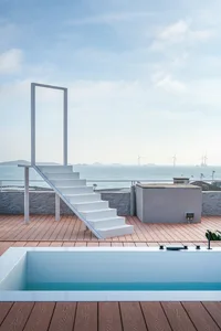 A minimalist pool deck featuring wooden stairs and a clear view of the ocean and wind turbines.