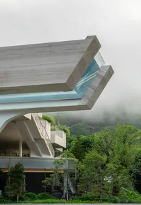 A modern architectural structure with a unique concrete design, featuring a cantilevered window and lush greenery.