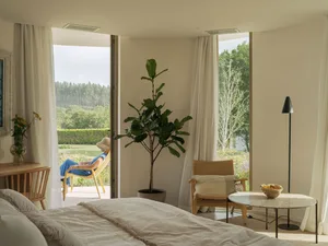 A modern bedroom featuring a cozy bed with white bedding, a wooden floor, and minimalist furniture.