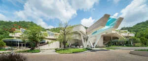 A modern concrete cliff house with a glass roof and outdoor greenery.