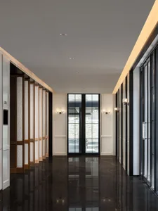 A minimalist corridor featuring dark marble flooring and walls, with sconces and large windows.