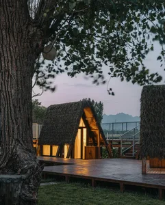 A charming cottage with a thatched roof illuminated during dusk hours, surrounded by a serene outdoor setting.