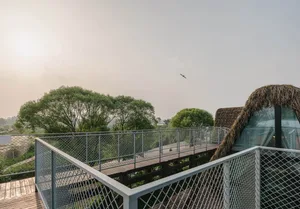A deck with a thatched roof and metal railing overlooking a tree-lined area.