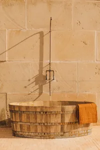 A wooden bathtub with a metallic shower hose against a beige stone wall and floor