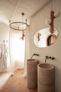 A minimalist bathroom featuring concrete sinks and wood flooring, with a white curtain and round mirror.