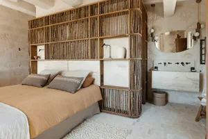 A minimalist bedroom featuring a wooden bed with beige bedding and a wall shelf made of wooden sticks.