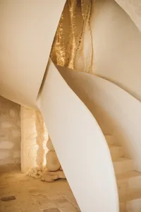 A minimalist interior space featuring a concrete staircase with a spiral design, leading to a residential area with a stone t