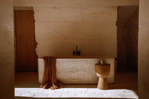 A minimalist bathroom with stone walls and a freestanding stone bathtub.