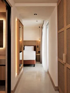 A minimalist bedroom with textured walls, light wood accents, and white fabric furnishings.