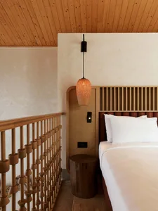 Minimalist bedroom featuring a wooden bed with a wooden headboard and a wooden bedside table with a woven pendant lamp.