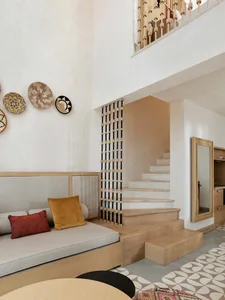 A modern living room featuring a concrete wall, patterned floor tiles, and a wooden sofa with yellow and red pillows.
