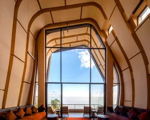 A modern living room with a large glass window showing a clear blue sky and distant views.