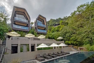 A modern, poolside lounge area with white umbrellas, lounge chairs, and a curved pool surrounded by greenery and modern archi