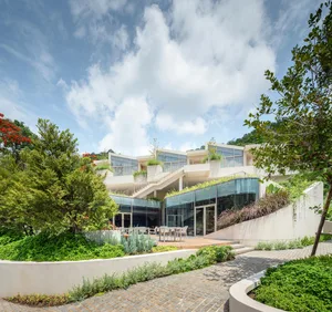 Modern residential building with a white concrete exterior, featuring large windows and greenery.