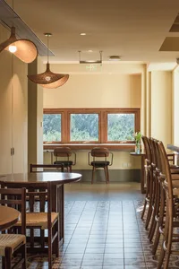 A minimalist restaurant interior with wooden furniture and large windows overlooking a green landscape.