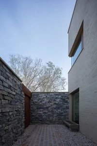 Modern house exterior with stone and brick walls, featuring a brick pathway and minimalist design.