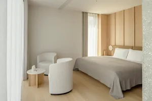 A minimalist bedroom with a circular desk chair, a circular side table, and a bed with a white shade.