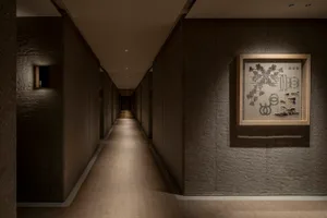 極簡走廊，牆面為質感混凝土，右側牆面懸掛藝術作品。