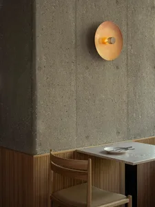 Minimalist restaurant interior featuring a concrete wall, wooden chair, and round gold light fixture.