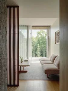 Modern minimalist living room with neutral-toned furniture and a view of greenery through large windows.