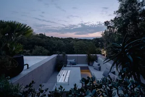 Modern outdoor lounge area with concrete, metal, and glass elements. Includes seating, cushions, and a fire pit.