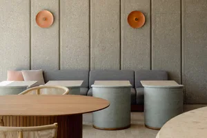 Modern restaurant interior with concrete walls, fabric seating, and wooden tables and stools.