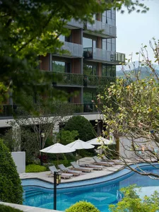 Modern swimming pool with concrete deck, surrounded by lush greenery and sunlight reflections.
