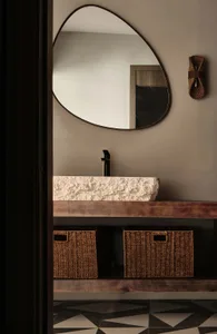 A modern bathroom with a stone vessel sink, wooden countertop, woven baskets, and a geometric floor.