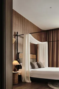 A modern minimalist bedroom features a white bed with curtains and a wooden headboard, set against a wooden wall.