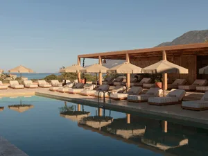 Swimming pool area with sun loungers, umbrellas, and a wooden canopy overlooking the sea.