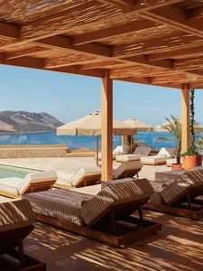 A minimalist poolside lounge area with wooden beams and sun loungers.