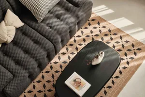 A modern living room with a black sofa, patterned rug, and black coffee table with a book and vase.