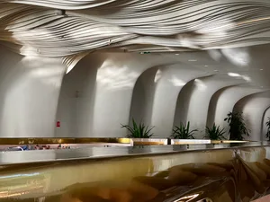 Exposed metallic ceiling with curved, wavy lines, featuring a modern, industrial design with geometric shapes and minimalist 