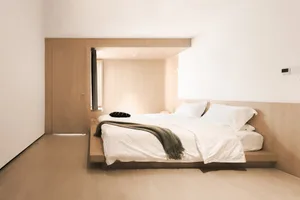 A minimalist bedroom with a floating bed platform, wooden walls, and a simple arrangement of pillows and a blanket.