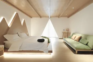 A minimalist bedroom featuring a bed with a geometric headboard and a green couch, set against a white wall and a wooden ceil