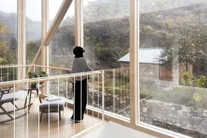 A minimalist interior design featuring large glass windows overlooking a natural landscape.