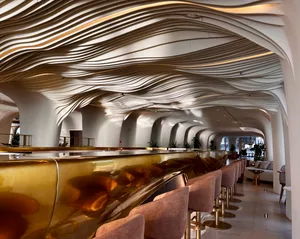 An elegant indoor bar area featuring a metallic counter and a wave-patterned ceiling.